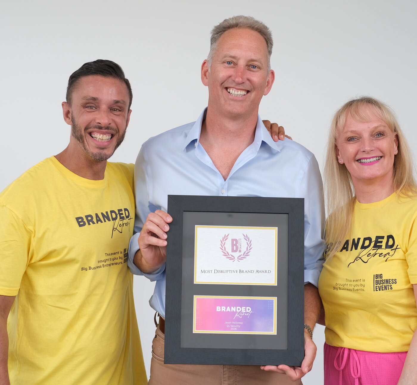 Jason Holloway of QL Security holding the Most Disruptive Brand Award, with the two Branded Retreat hosts either side